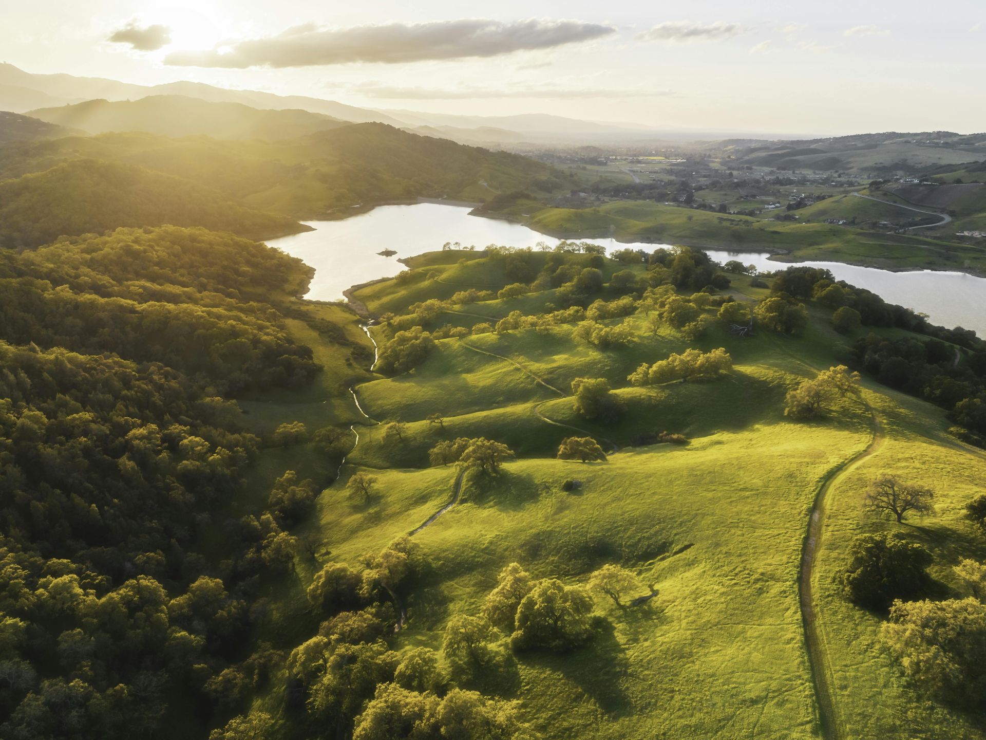Golden hour aerial view of rolling hills and lake in San Jose, California.